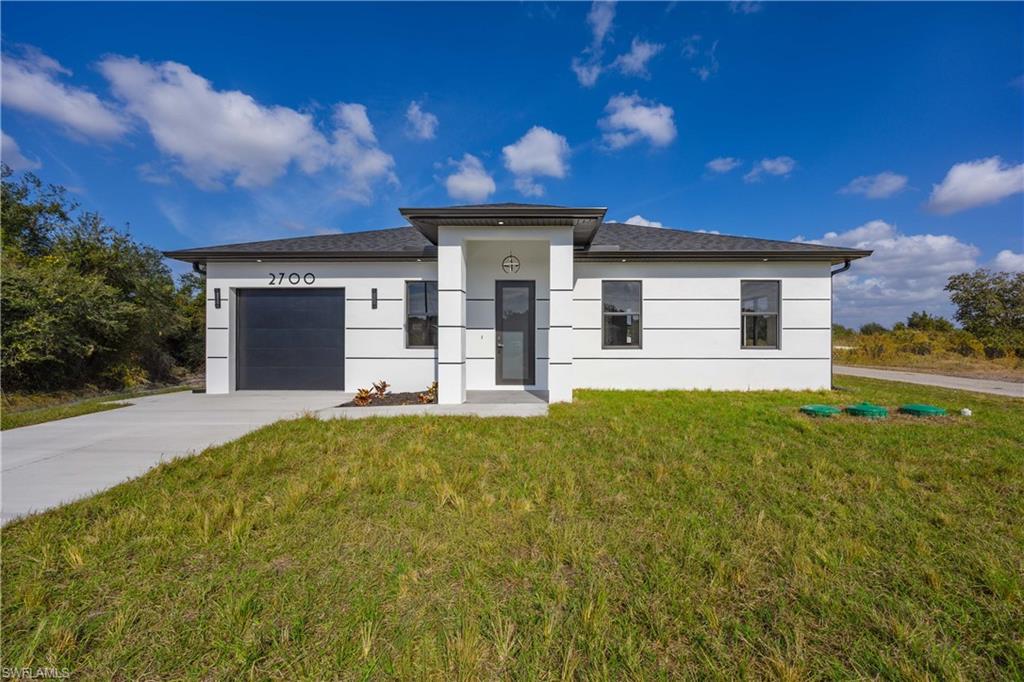 Prairie-style home with an attached garage, a front lawn, driveway, and stucco siding