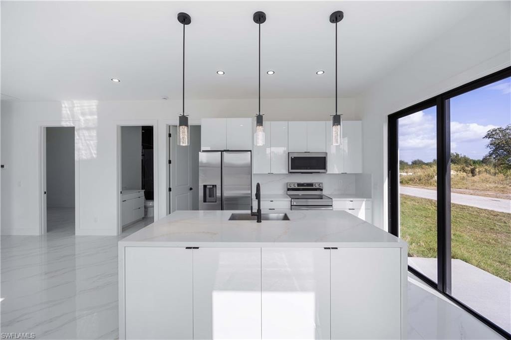 Kitchen with stainless steel appliances, white cabinets, light stone countertops, and hanging light fixtures