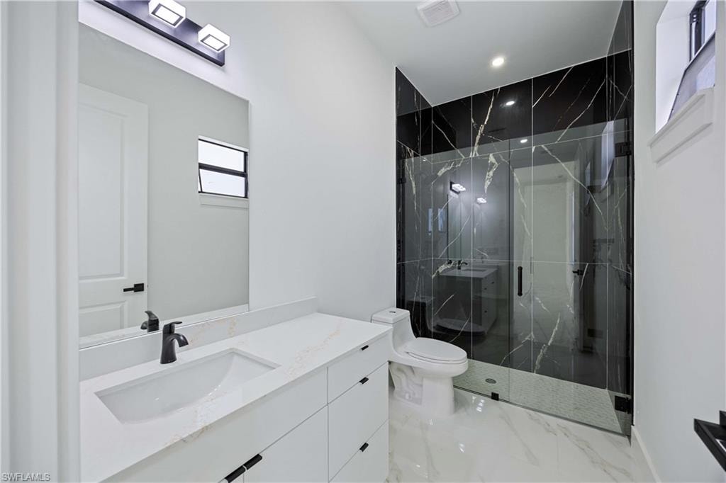 Bathroom featuring a marble finish shower, vanity, recessed lighting, and light marble finish floors