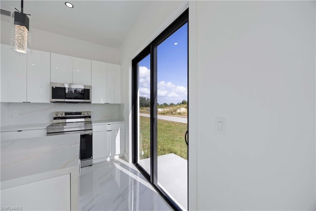 Kitchen with stainless steel appliances, modern cabinets, white cabinets, pendant lighting, and light marble finish floors
