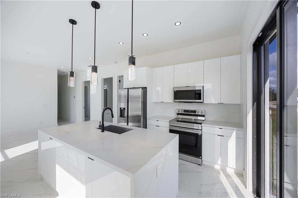Kitchen with stainless steel appliances, white cabinetry, an island with sink, light stone counters, and modern cabinets