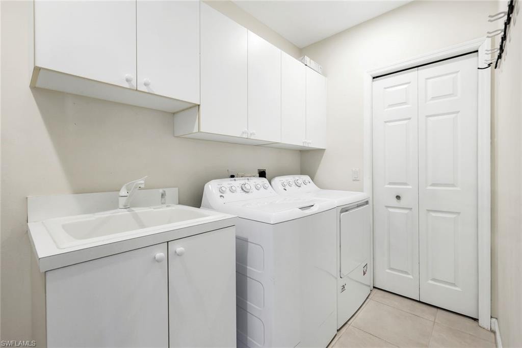 Laundry area featuring cabinet space, Utility sink, light tile patterned floors, with washing machine and dryer.