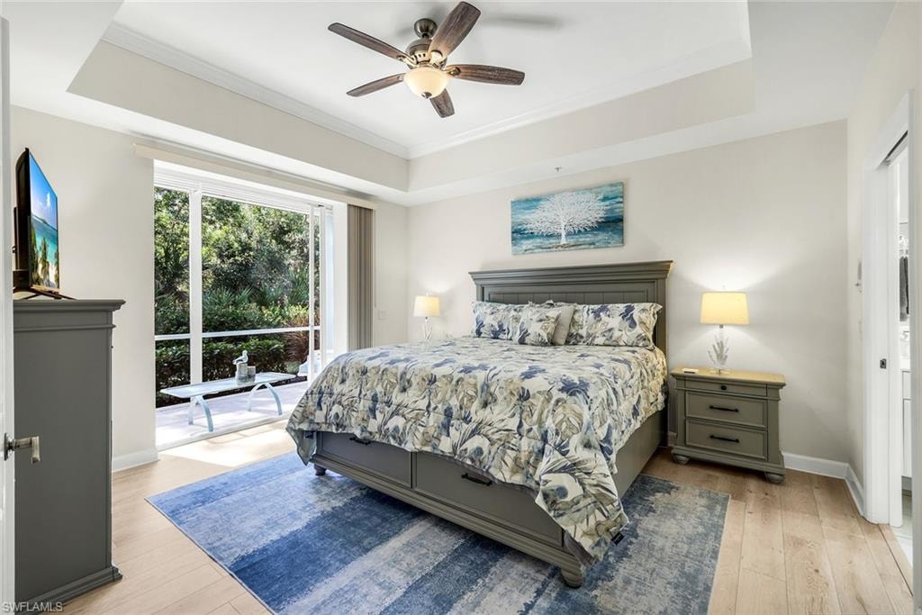 Primary Bedroom featuring a tray ceiling, light wood-type tile flooring, and ornamental molding. View of sliders looking into rear Lanai.