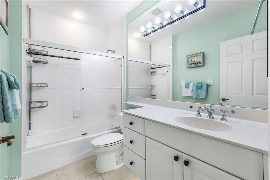 Guest bathroom with vanity, light tile patterned flooring, and shower / bath combination with glass door.