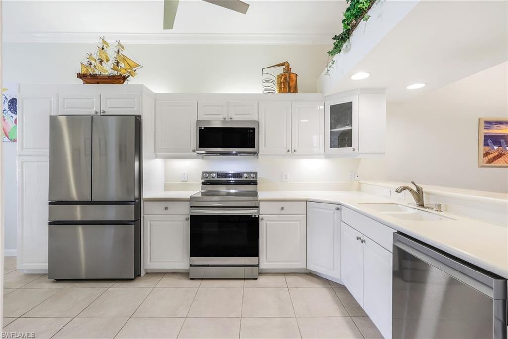 Kitchen with stainless steel appliances, light Corian countertops, light tile patterned floors, white cabinets, and recessed lighting