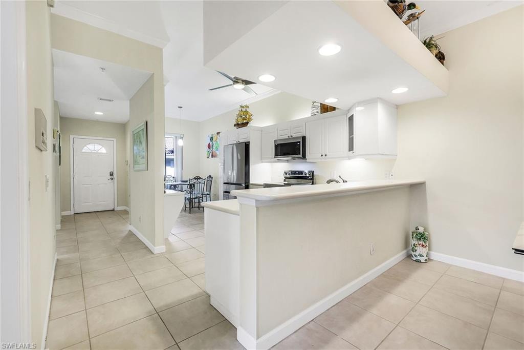 Kitchen with white cabinets, light tile patterned flooring, a peninsula breakfast bar, appliances with stainless steel finishes and recessed lighting.