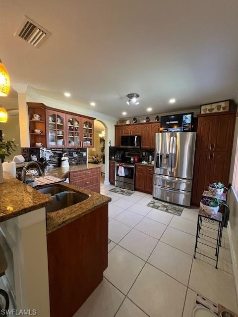 Kitchen featuring arched walkways, glass insert cabinets, dark stone counters, ornamental molding, and stainless steel appliances