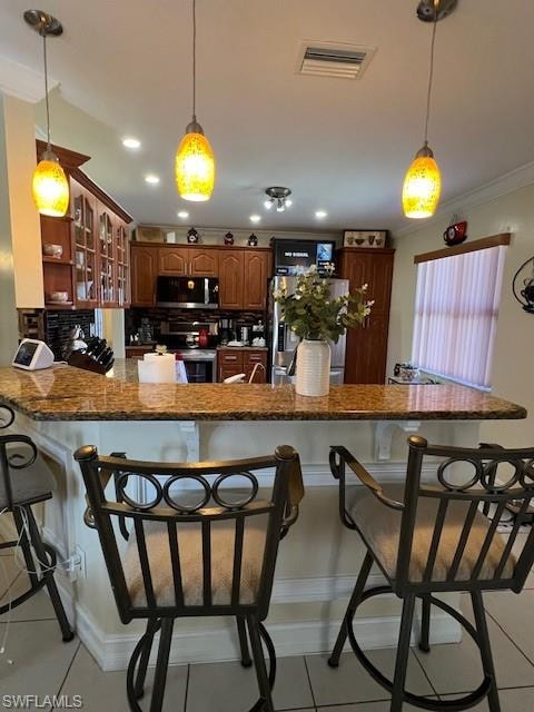 Kitchen featuring a kitchen breakfast bar, decorative light fixtures, stainless steel appliances, crown molding, and light tile patterned floors