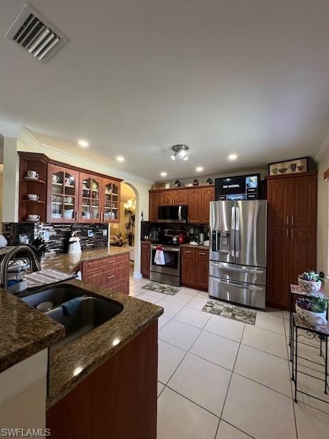 Kitchen with arched walkways, crown molding, glass fronted cabinets, stainless steel appliances, and tasteful backsplash