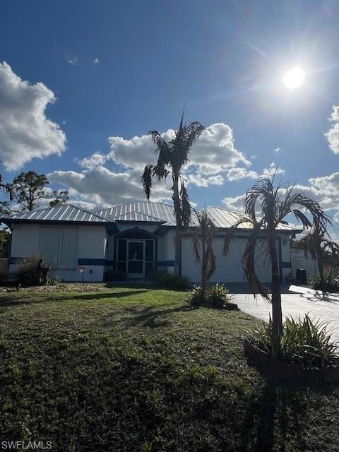 View of front of property featuring an attached garage, driveway, a front lawn, and a metal roof