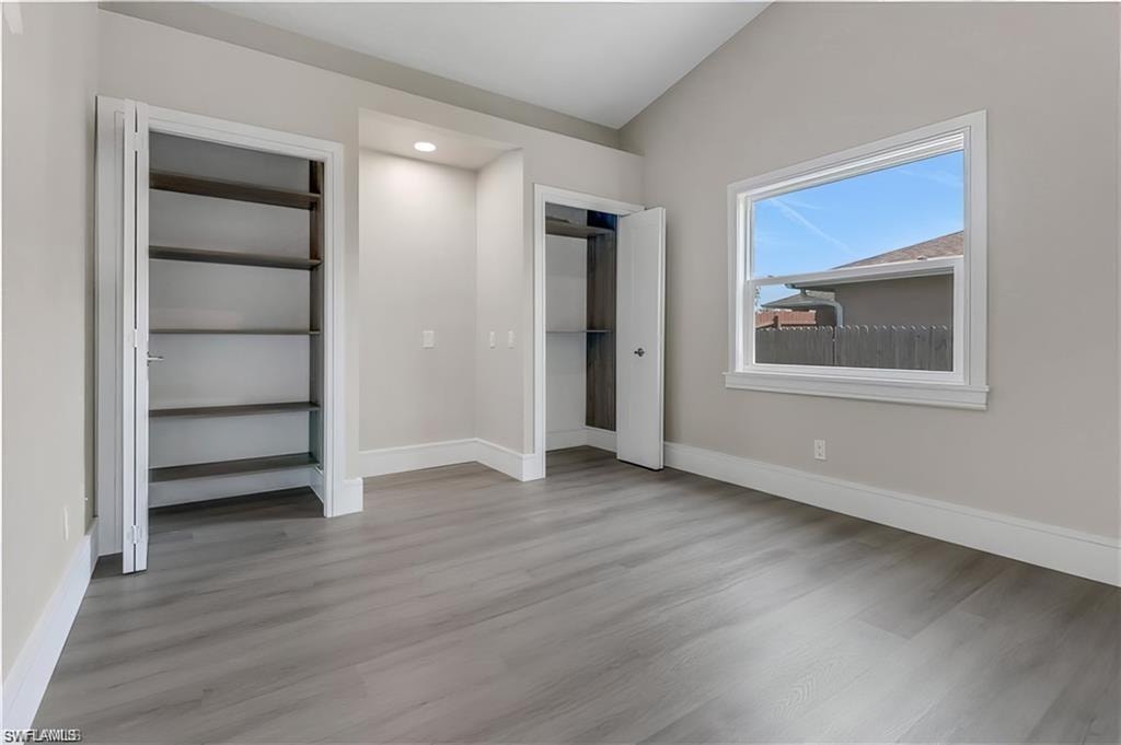 Unfurnished bedroom with vaulted ceiling, multiple closets, and light wood-type flooring