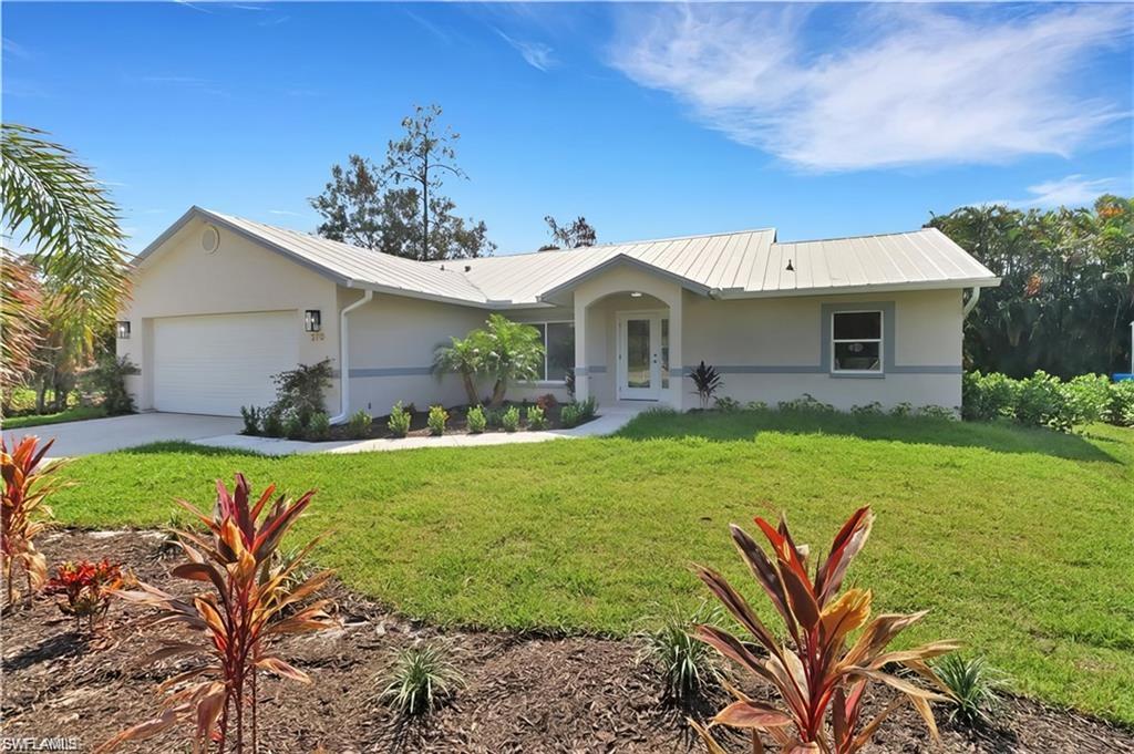 Ranch-style home with a garage, stucco siding, a front lawn, driveway, and a metal roof