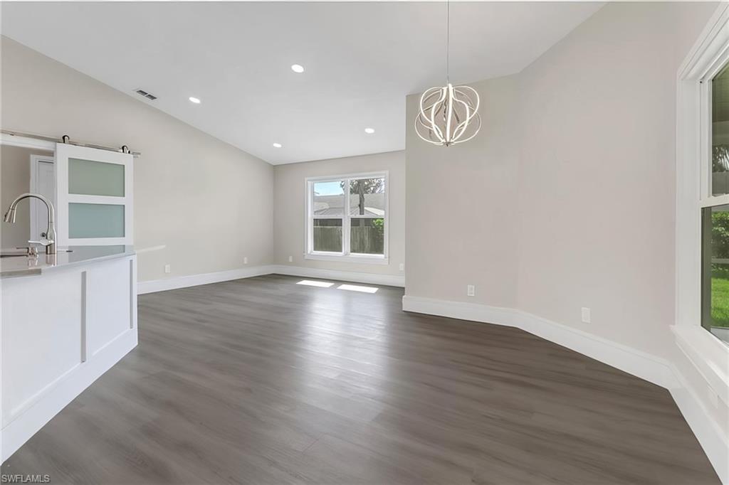 Unfurnished dining area with dark wood-style floors, a chandelier, a barn door, and vaulted ceiling
