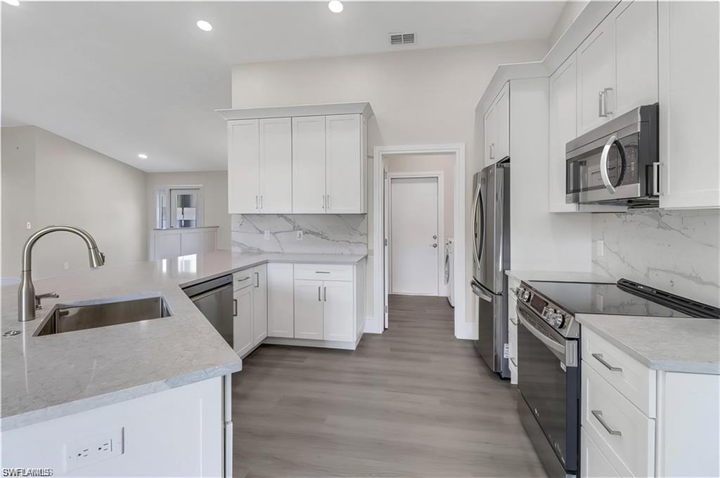Kitchen featuring stainless steel appliances, a peninsula, white cabinetry, and recessed lighting