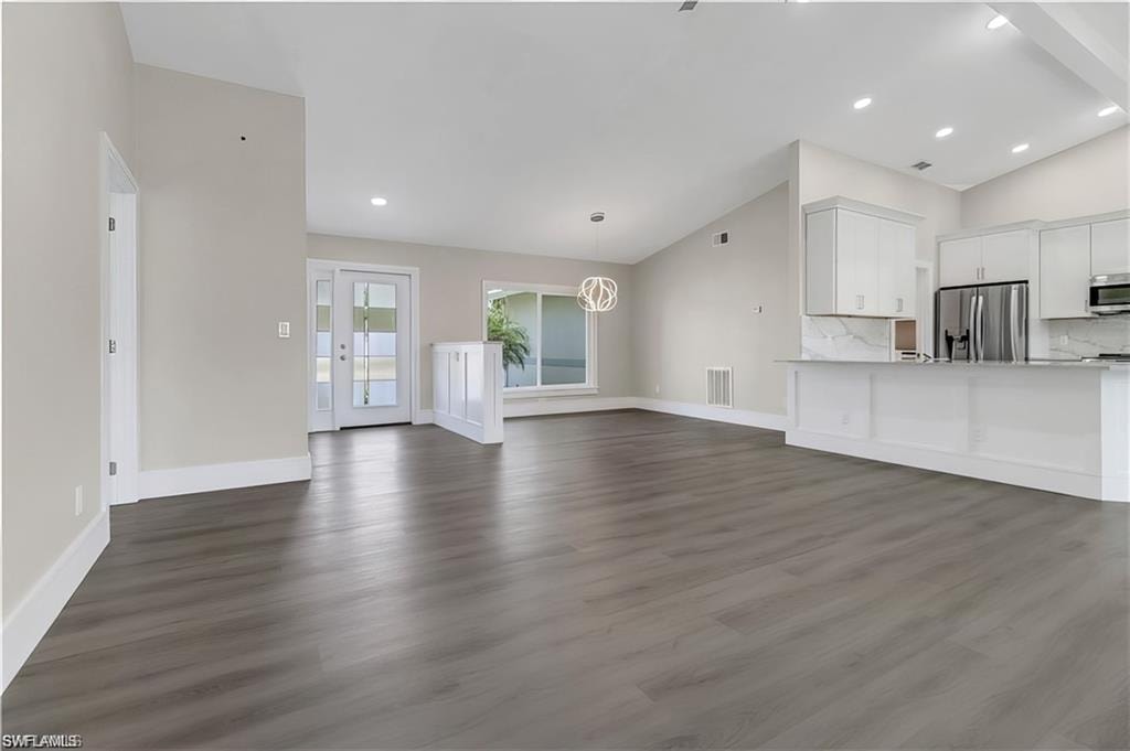 Unfurnished living room featuring vaulted ceiling, dark wood-style floors, and a chandelier