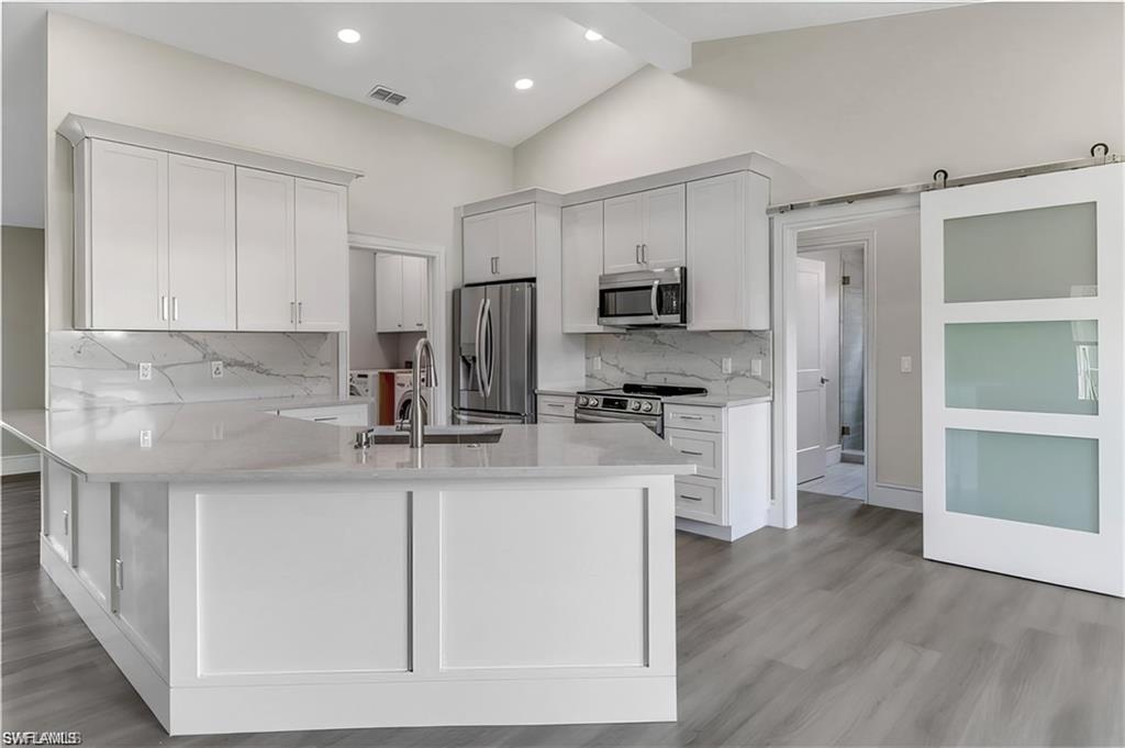 Kitchen with a peninsula, a barn door, white cabinetry, light stone counters, and stainless steel appliances