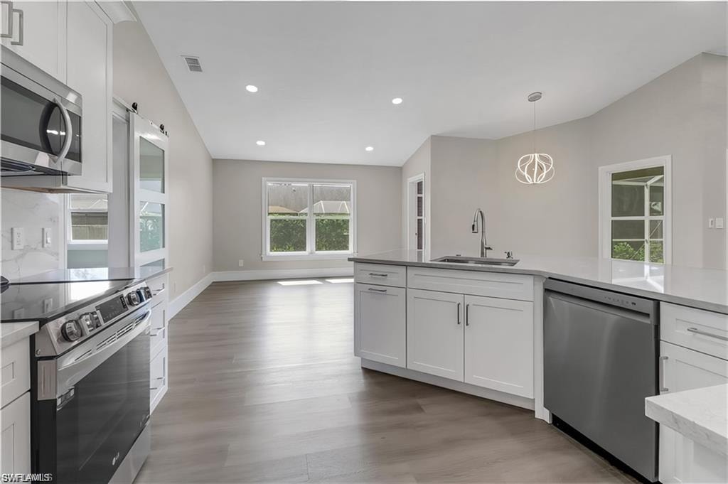 Kitchen with stainless steel appliances, white cabinets, light stone counters, a barn door, and hanging light fixtures