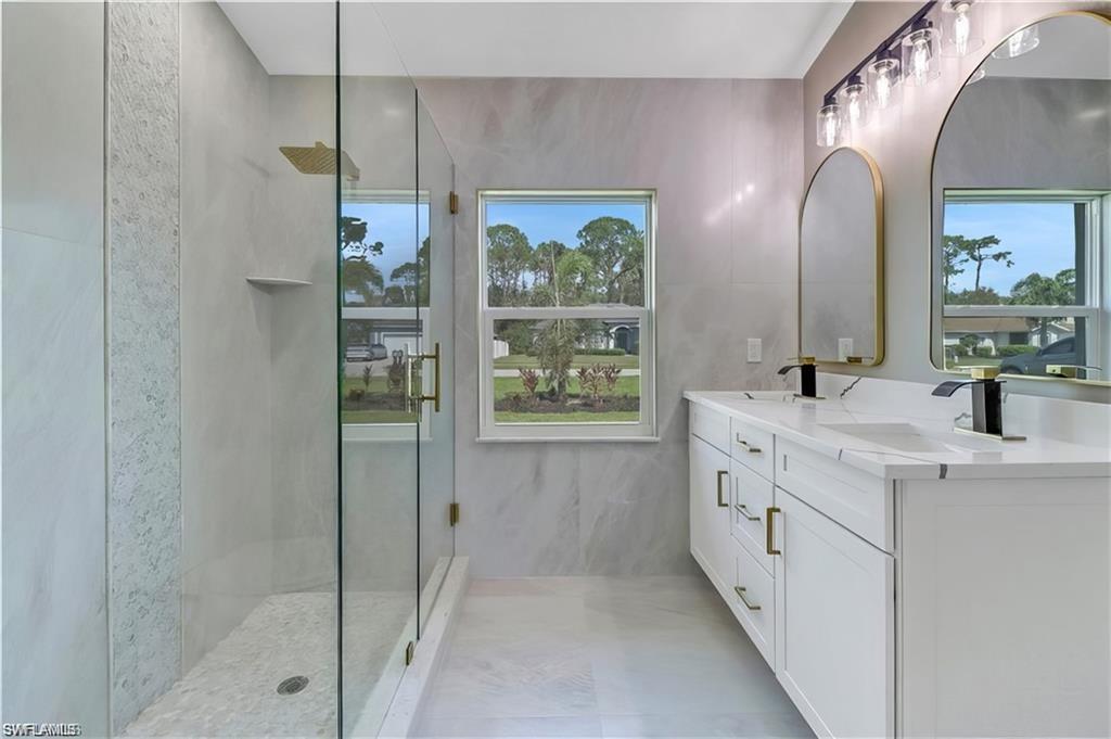 Full bath featuring double vanity and a marble finish shower
