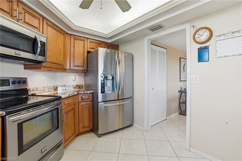 Kitchen with stainless steel appliances, wood finish cabinetry, light stone countertops, ceiling fan, and crown molding - Virtually Edited Image