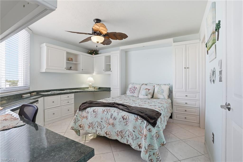 Bedroom with light tile patterned floors, ceiling fan, and built in study area - Virtually Edited Image