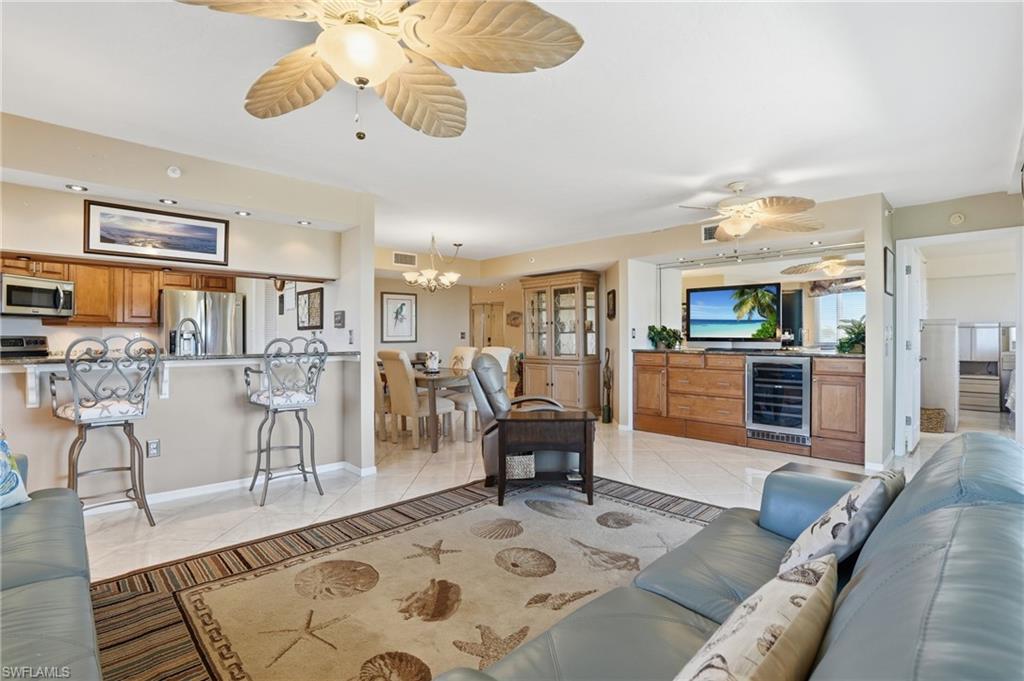 Living room featuring a ceiling fan, wine cooler, light tile patterned floors, and suspended lighting - Virtually Edited Image