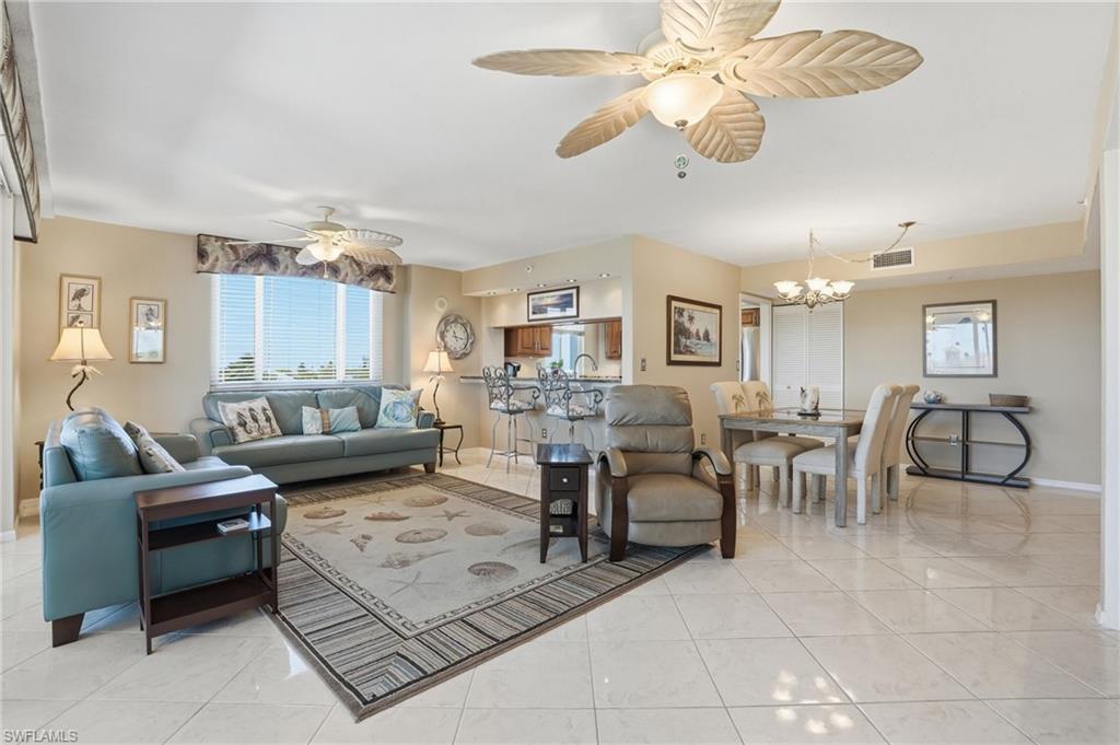Living area with a ceiling fan, hanging lights, and light tile patterned floors - Virtually Edited Image