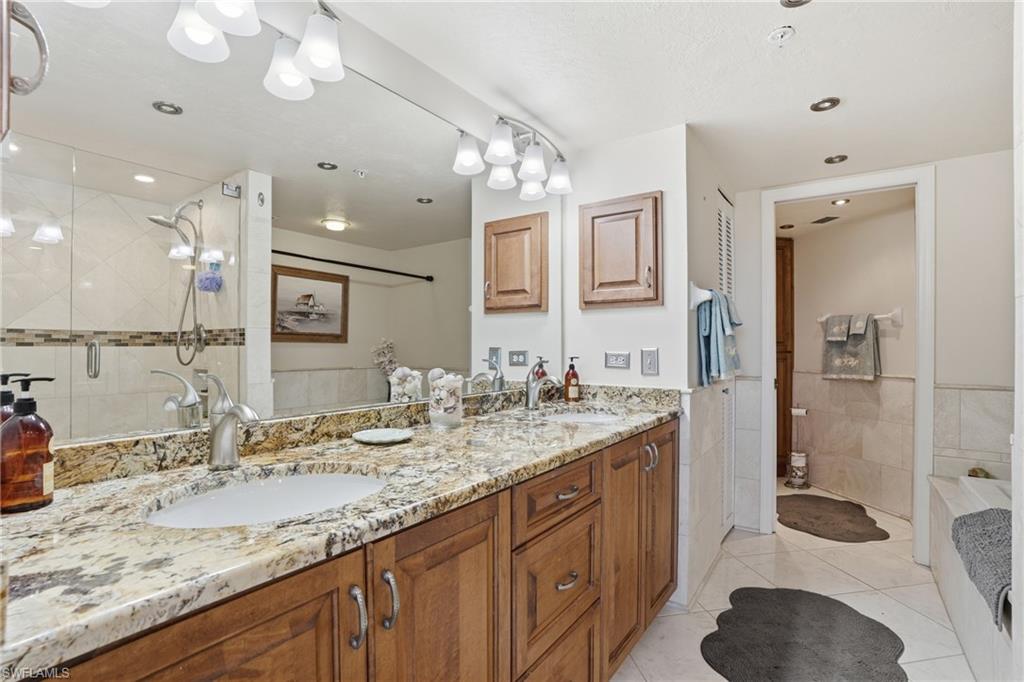 Full bathroom featuring double vanity, light tile patterned floors, a garden tub, a shower stall, and tile walls - Virtually Edited Image