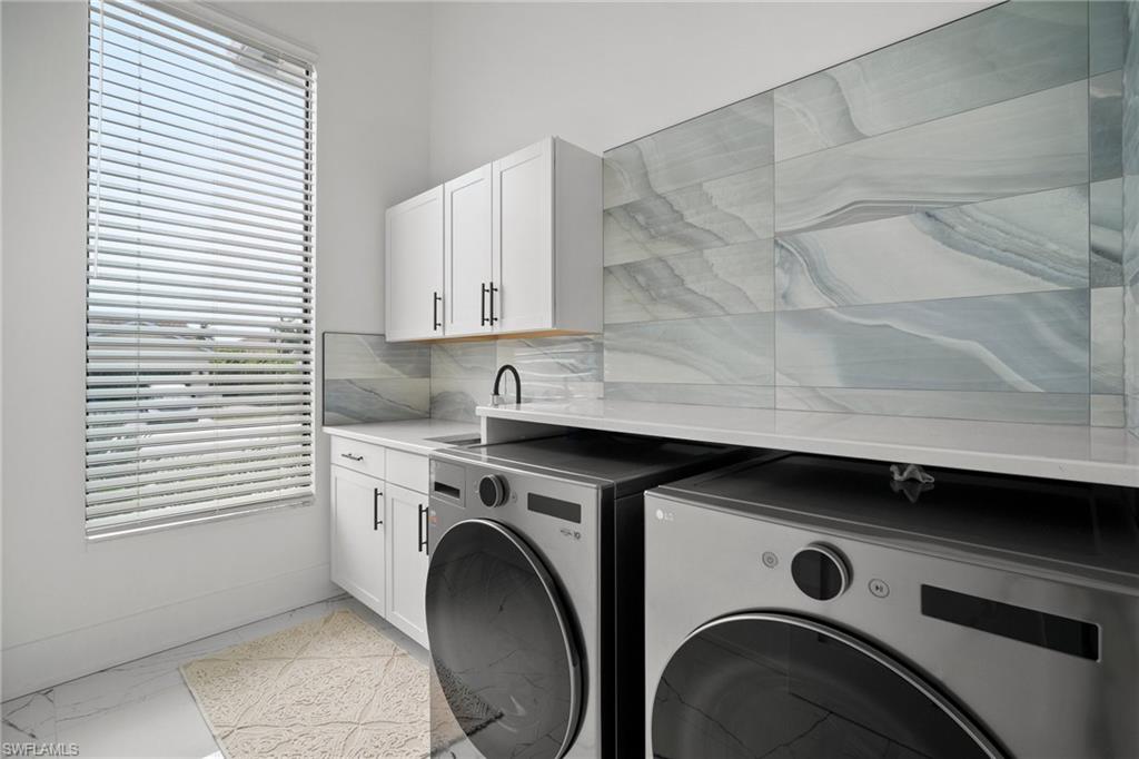 Clothes washing area featuring cabinets, washer and clothes dryer, and a healthy amount of sunlight