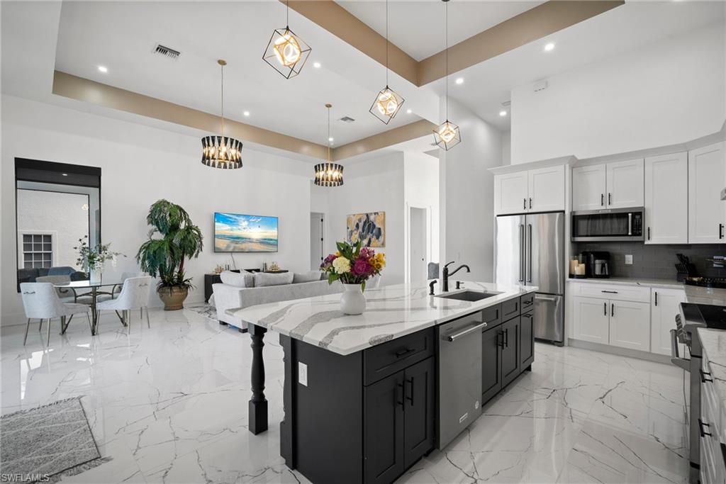 Kitchen with a tray ceiling, white cabinets, pendant lighting, and appliances with stainless steel finishes