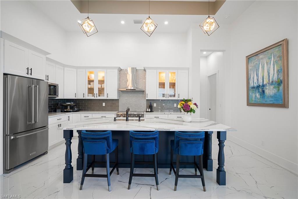 Kitchen with appliances with stainless steel finishes, white cabinetry, wall chimney exhaust hood, and an island with sink