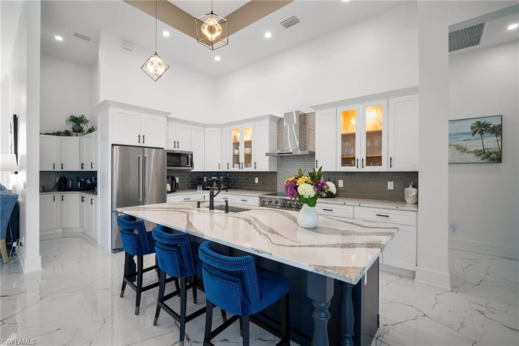 Kitchen with white cabinets, an island with sink, wall chimney range hood, and appliances with stainless steel finishes