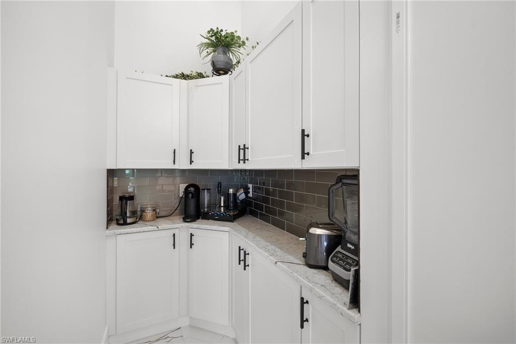 Bar with white cabinets, light stone countertops, and tasteful backsplash