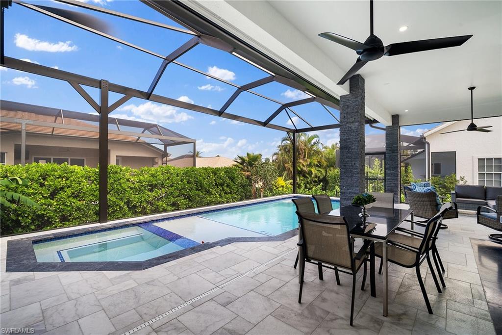 View of pool with glass enclosure, ceiling fan, and a patio area