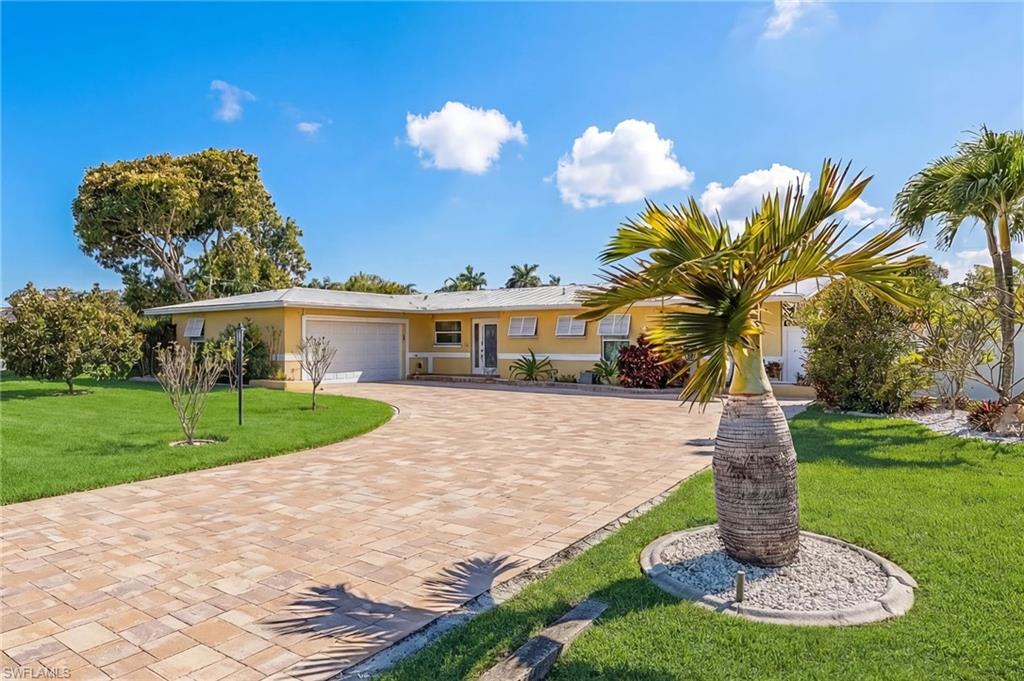Ranch-style house featuring a front yard, stucco siding, an attached garage, and decorative driveway