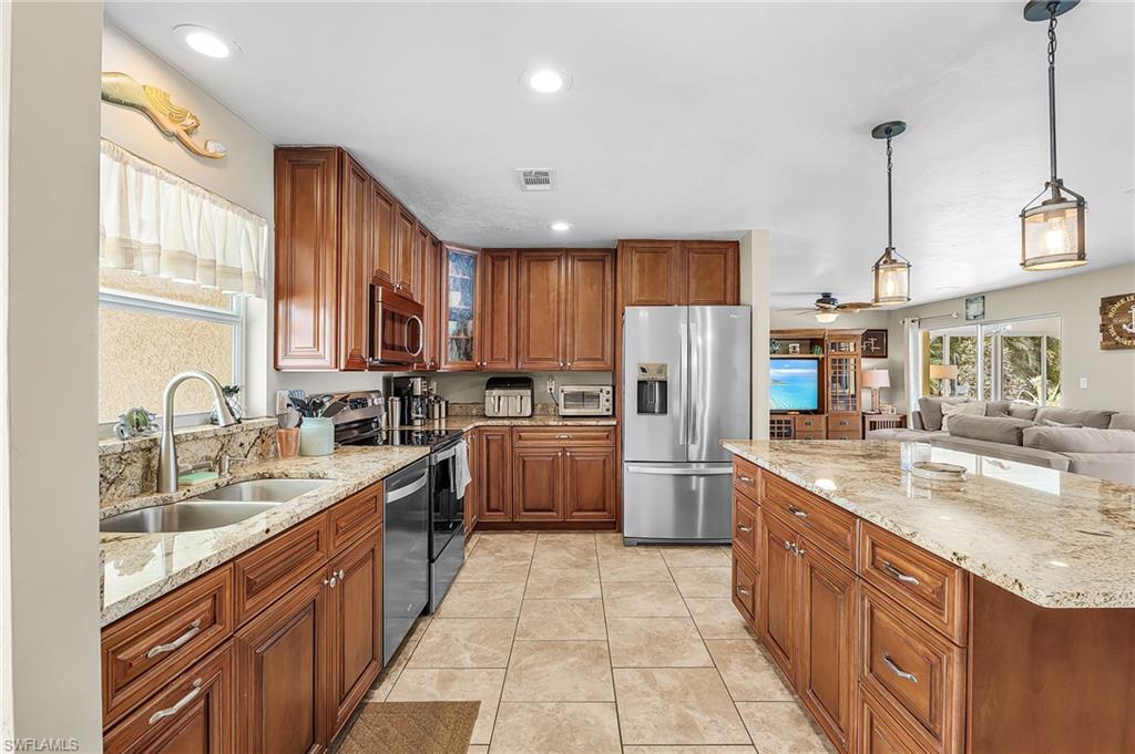 Kitchen featuring wood finish cabinetry, stainless steel appliances, light stone counters, open floor plan, and glass insert cabinets