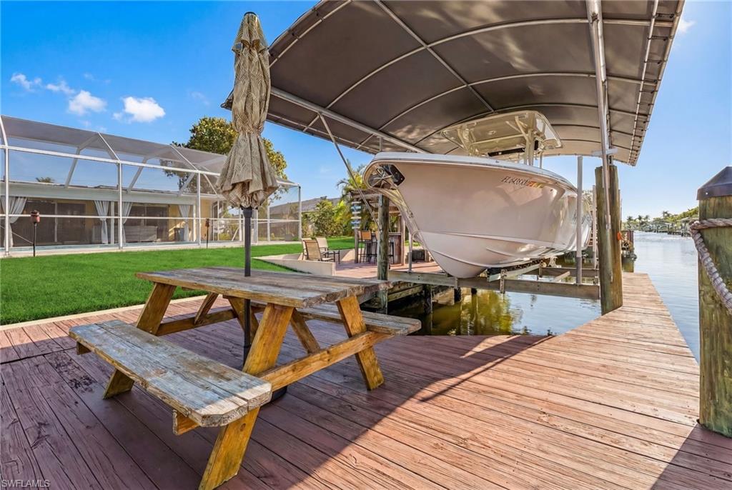 Dock area with boat lift, a sunroom, a lanai, a lawn, and a water view