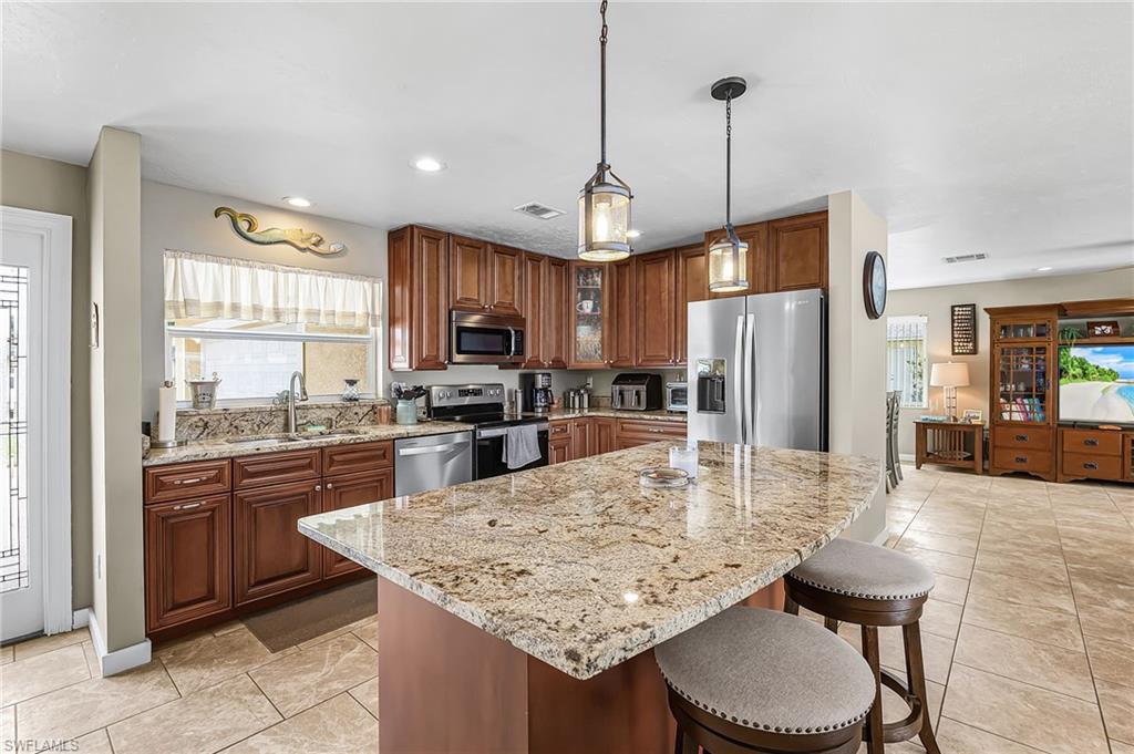 Kitchen with stainless steel appliances, light stone counters, a breakfast bar, wood finish cabinetry, and hanging light fixtures