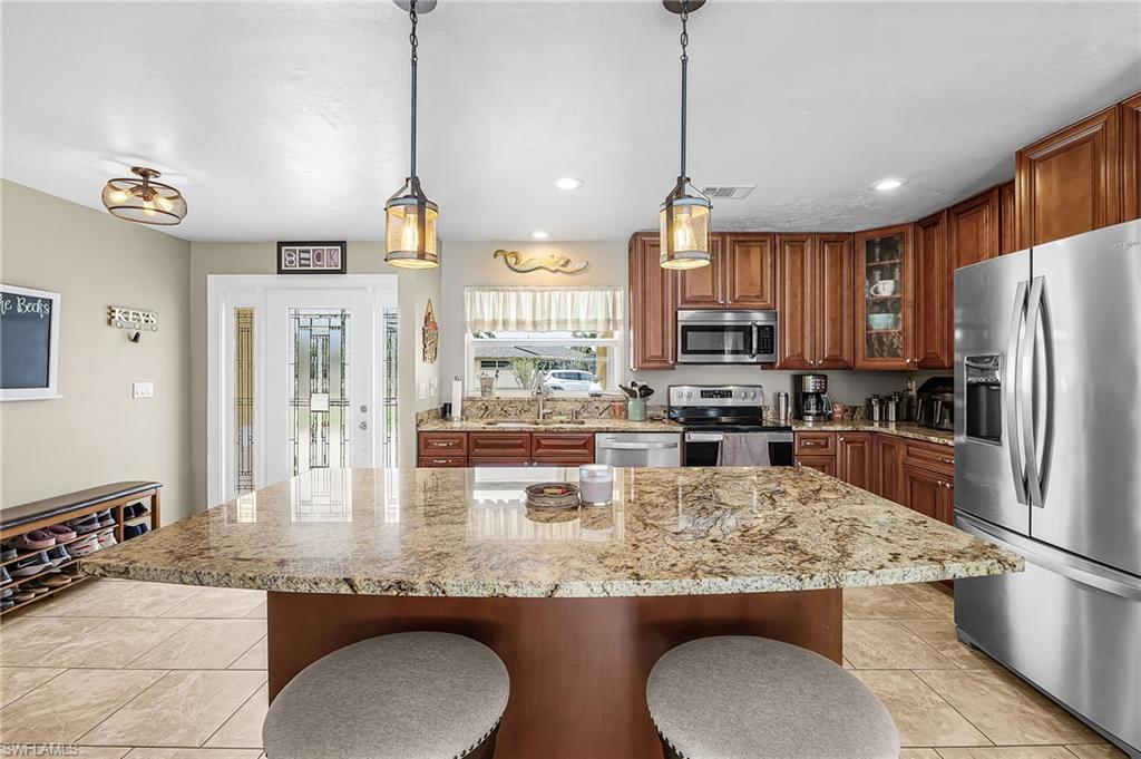 Kitchen with stainless steel appliances, wood finish cabinetry, light stone countertops, glass fronted cabinets, and a kitchen bar