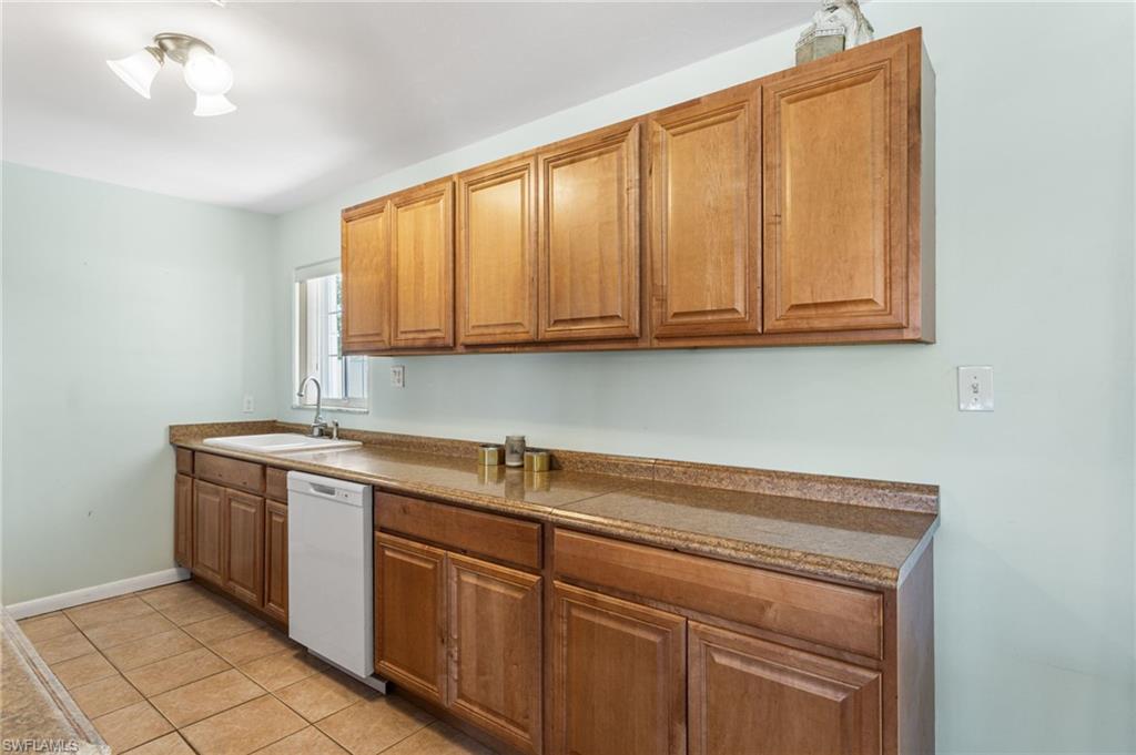 Kitchen featuring dishwasher, light tile patterned floors, wood finish cabinetry, and dark countertops