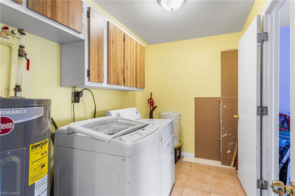 Laundry room featuring electric water heater, cabinet space, washer and dryer, and light tile patterned flooring