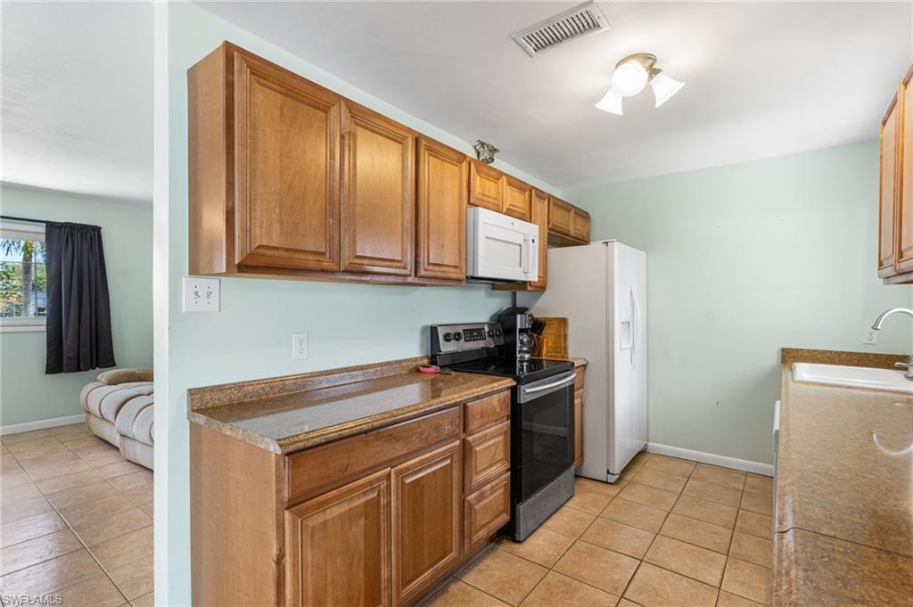 Kitchen with white appliances, wood finish cabinetry, light tile patterned floors, and dark countertops