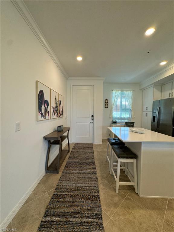 Kitchen with a kitchen bar, ornamental molding, black fridge with ice dispenser, and light tile patterned flooring