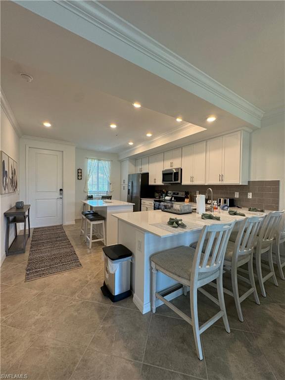 Kitchen featuring white cabinetry, appliances with stainless steel finishes, kitchen peninsula, backsplash, and a breakfast bar area