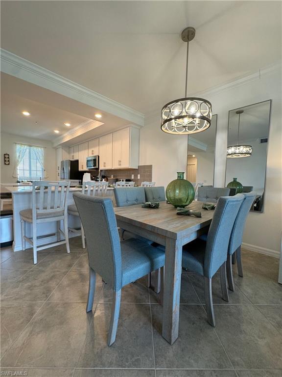 Tiled dining area with a notable chandelier, a raised ceiling, and ornamental molding