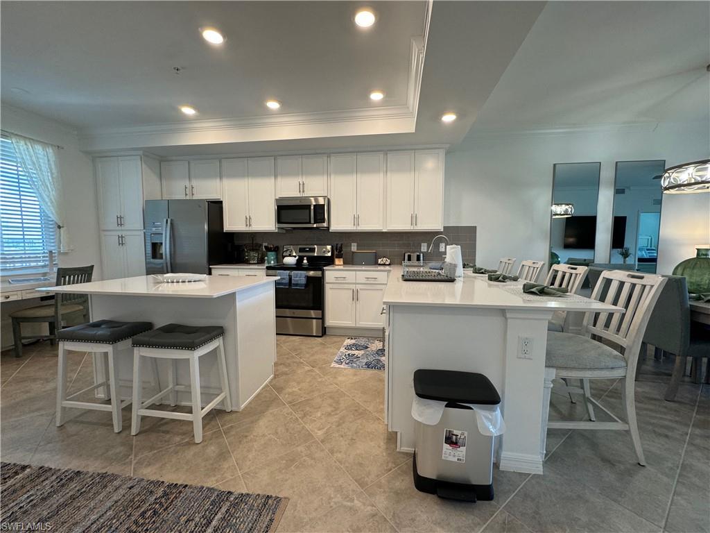 Kitchen with white cabinetry, appliances with stainless steel finishes, kitchen peninsula, light tile patterned floors, and a breakfast bar