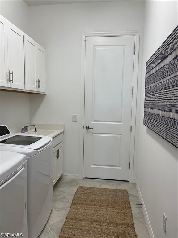 Laundry room featuring cabinets, sink, light tile flooring, and washing machine and clothes dryer