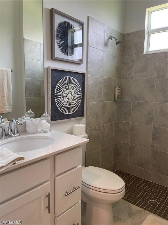 Bathroom with a tile shower, tile flooring, large vanity, and toilet