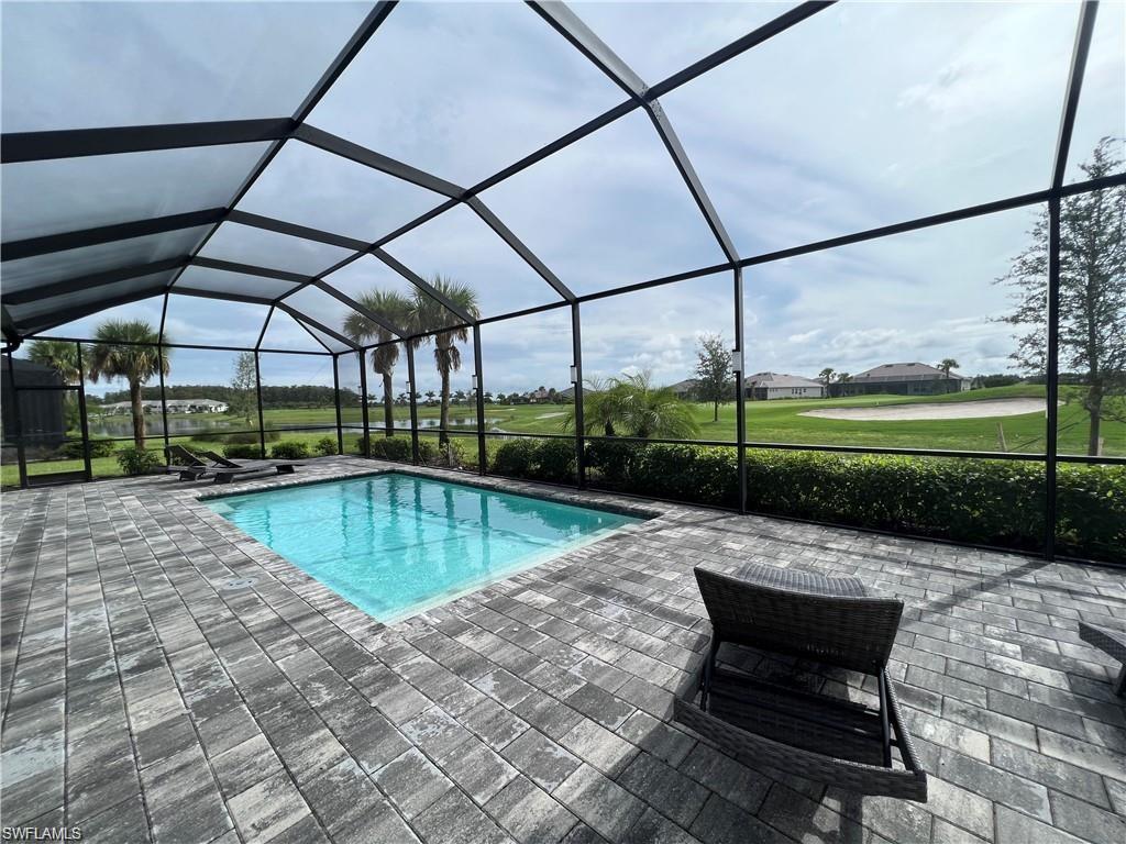View of pool with enclosure, a patio area, and a lawn