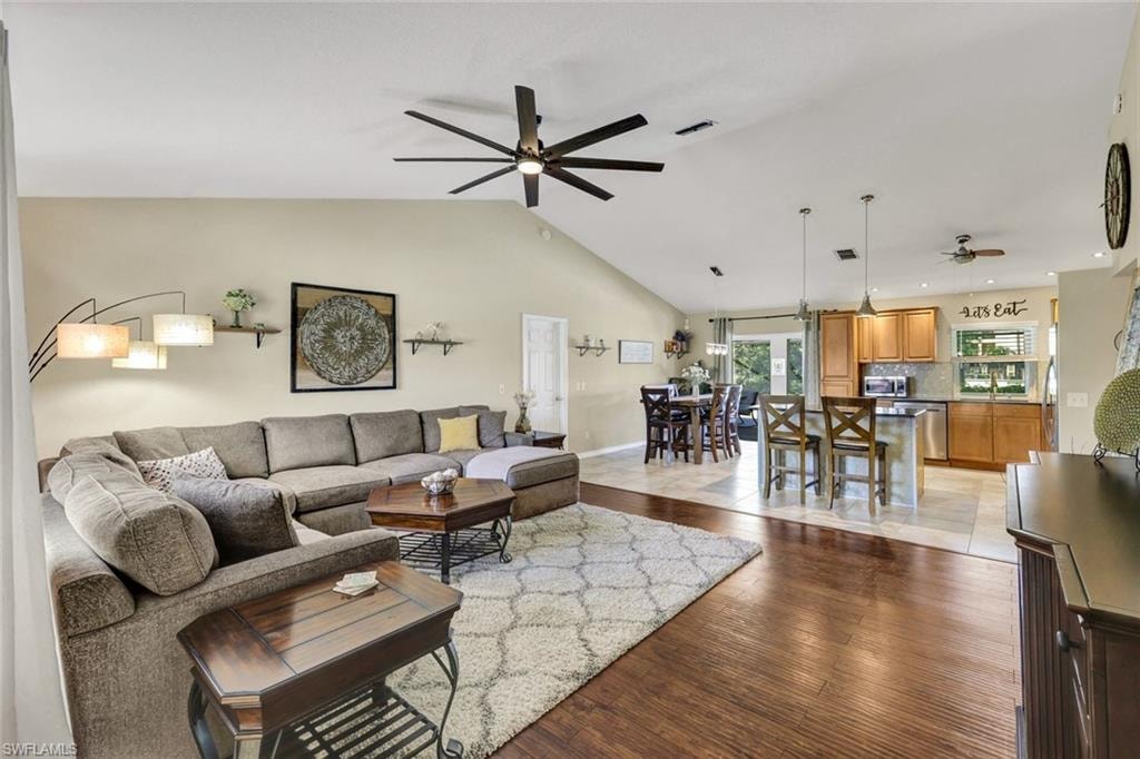Living area with dark wood-style flooring, a ceiling fan, and vaulted ceiling