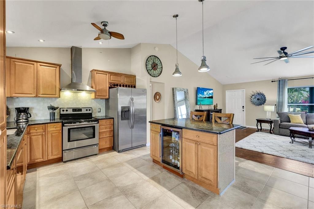 Kitchen featuring ceiling fan, stainless steel appliances, wine cooler, wood finish cabinetry, and vaulted ceiling